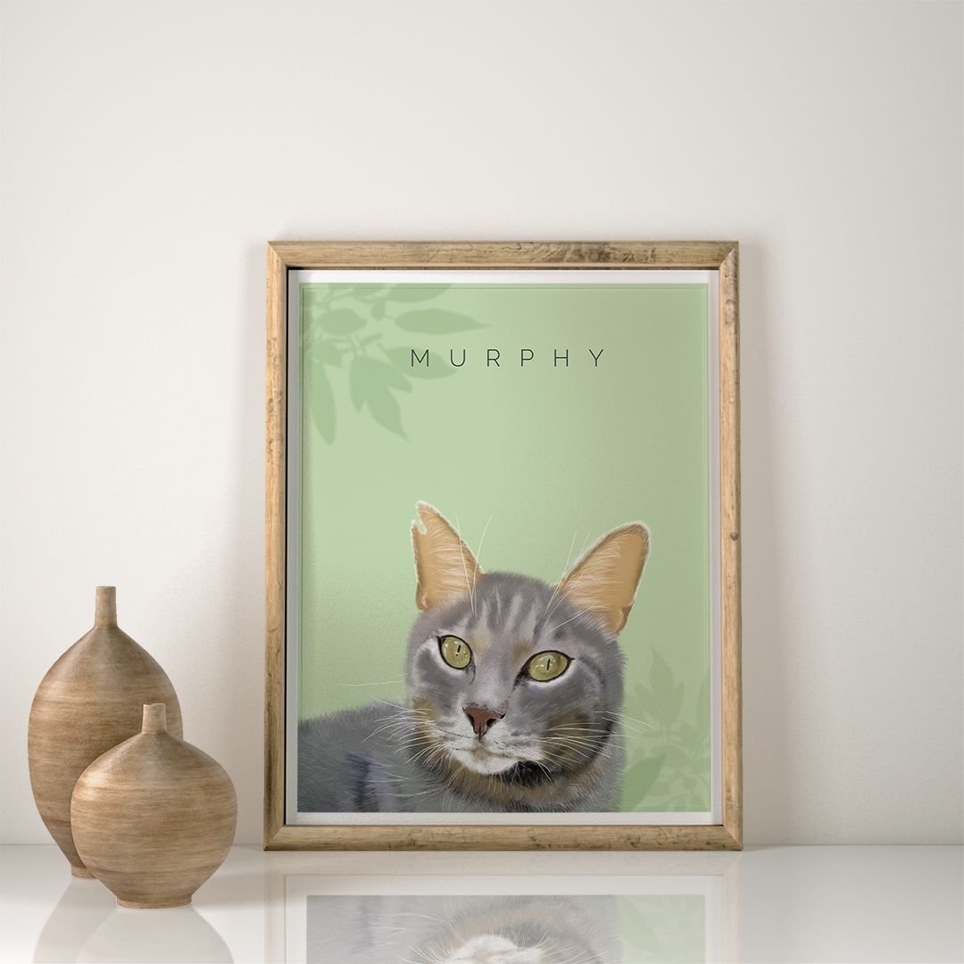 La "Ilustración Personalizada" es un retrato enmarcado de un gato gris de ojos verdes, con la etiqueta "Murphy", sobre un fondo verde claro. Reposa sobre un estante blanco junto a dos jarrones de madera.